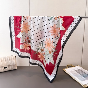 Detailed view of floral polka dot silk scarf draped on a metal stand with a bag