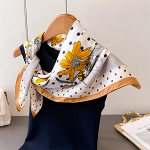 Detailed texture of white silk scarf with sunflower print and black polka dots on blue vest