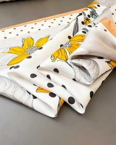 Detailed view of floral silk scarf featuring yellow blossoms, black polka dots and orange edges