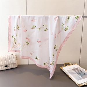 Détail d'un carré de soie à fleurs et bordure rose à côté d'un sac à main matelassé