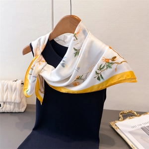 Détail d'un foulard floral en soie avec fleurs orange et bordure jaune sur haut noir
