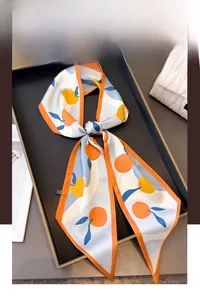 Close-up of a blue citrus print silk twilly scarf tied in a bow on a minimalist tray