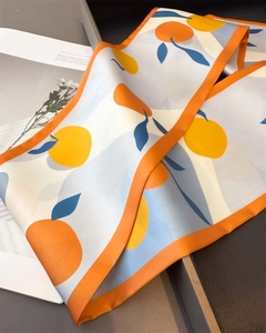 Macro detail of silk scarf with orange fruit patterns and blue leaves on a white base