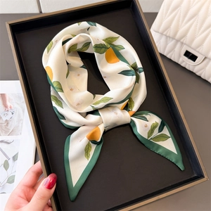 Silk-like scarf with lemon and leaf print, tied in a knot on a black tray display