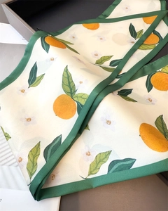 Close-up of summer silk scarf featuring orange and floral patterns with green edges