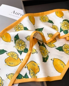 Detail of silk scarf with lemon pattern on gray tray showing fine texture and orange hem