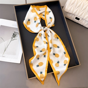Long white silk scarf with yellow pineapple prints draped over a stylish handbag
