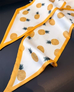 Detail of a long narrow silk scarf with vibrant orange pineapple print on white