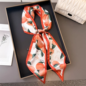 Long silk-like scarf with orange fruit print and red border tied on black tray