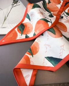 Detail of a silky long fruit print scarf with orange contrast piping on a desk