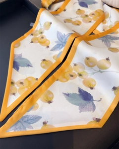 Close-up of silk twilly scarf with orange edges and botanical yellow berry print
