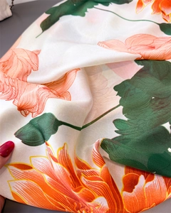 Macro detail of high-quality satin scarf with vibrant orange lotus and green leaf print