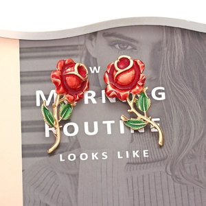Detail of red enamel rose earrings with golden stem and green leaves on a magazine