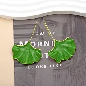 Boucles d'oreilles pendantes feuille de ginkgo dorée et émail vert sur un magazine