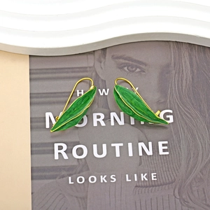 Détail de boucles d'oreilles feuille verte avec bordure dorée et émail marbré