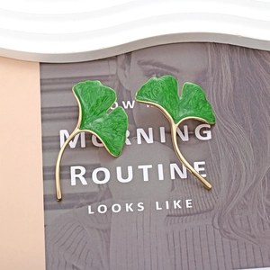 Ginkgo leaf drop earrings with green enamel and gold finish on a fashion magazine background
