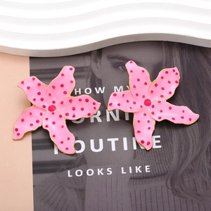 Boucles d'oreilles fleurs roses à pois avec bordure dorée sur fond de magazine