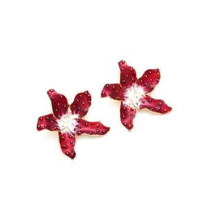 Détail macro de boucles d'oreilles fleur en émail rouge foncé avec granulés dorés