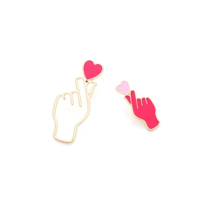 Macro shot of asymmetric heart gesture earrings with vibrant enamel finish and gold edges