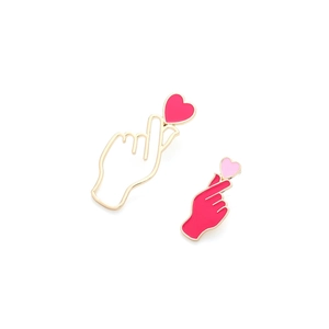 Detail of asymmetric gold heart gesture earrings with red and pink enamel finish