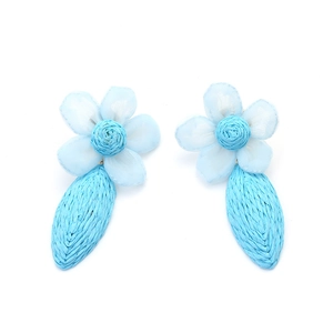 Détail de boucles d'oreilles fleurs en raphia bleu clair et tulle sur fond blanc épuré
