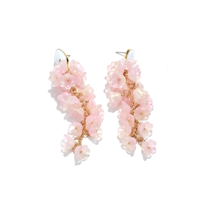 Dettaglio di orecchini lunghi con nappe, fiori rosa e catenine in metallo dorato