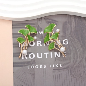 Elegant ginkgo leaf earrings with green enamel, gold plating, and pearls on a magazine