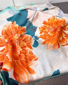 Detail of silk satin scarf featuring orange floral patterns and teal rolled edges
