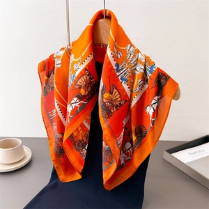 Elegant orange silk-like scarf with carriage print hanging on a wooden hanger