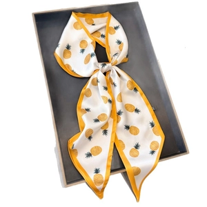 Long silk-like scarf with yellow pineapple patterns tied as a bow on a gray tray