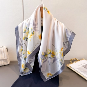 Foulard en soie ivoire à fleurs avec bordures grises drapé sur un pull bleu marine