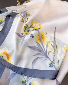 Texture détaillée d'un foulard en soie satinée avec imprimé floral jaune et bords bleus
