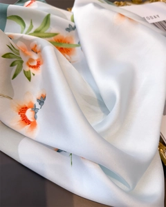 Détail d'un foulard en soie synthétique bleu clair avec imprimés floraux orange et brillant