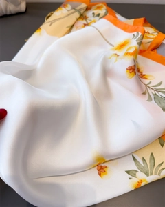 Détail d'un foulard en soie à fleurs montrant la texture douce et l'ourlet orange