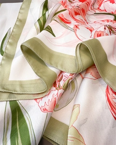 Detail of silk scarf showing vibrant lily print, smooth texture, and green rolled edges