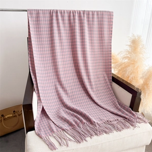 Detailed view of pink and grey houndstooth scarf with elegant long fringe on a sofa