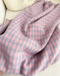 Close-up of pink and grey houndscaf check scarf with tassels on a soft beige sofa