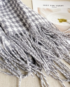 Detail of grey houndstooth scarf with soft fringe tassels on beige textured fabric