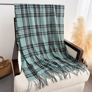 Detail of mint green plaid scarf with fringe on white sofa and leather bag background