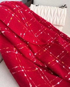 Close-up detail of soft red plaid scarf texture with elegant white handbag on a sofa