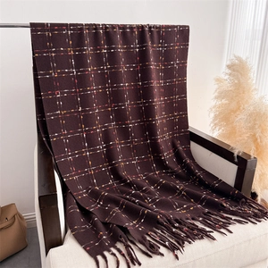 Detailed close-up of dark brown plaid cashmere scarf with soft fringes on a cozy chair