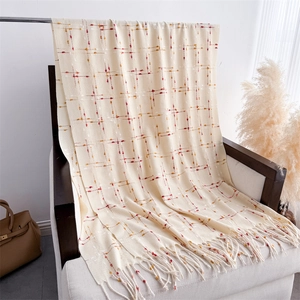 Detail of soft cream knitted scarf featuring red and yellow grid pattern and long tassels