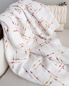 Detail of white scarf with orange plaid pattern and fringe on a soft sofa