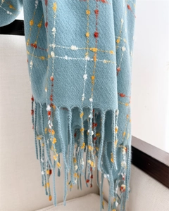 Macro detail of light blue checkered scarf featuring colorful dots and long fringe edges