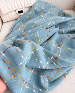 Close-up of light blue plaid scarf with fringes on a quilted bag background
