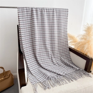 Detail of soft gray and white plaid scarf with fringe tassels on a decorative chair