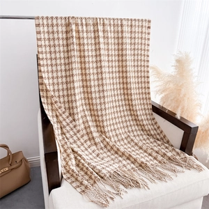 Gros plan d'une écharpe pied-de-poule beige à franges posée sur une chaise blanche