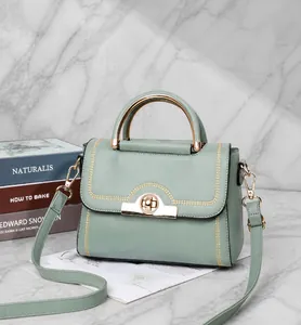 Detail einer mintgrünen Handtasche mit goldenem Halbmondgriff und edlem Drehverschluss