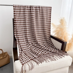 Détail de la texture d'une écharpe pied-de-poule avec franges sur un fauteuil