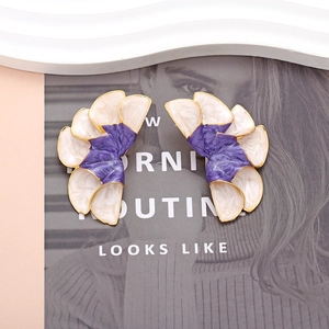 Orecchini a fiore in smalto viola e bianco con bordi dorati su rivista di moda